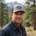 Man outdoors wearing a mens heather black Ghost Rack deer hunting trucker hat with antler logo on the front